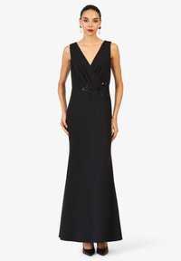 Robe de soirée noire avec un décolleté en V profond, design sans manches et détails en dentelle perlée à la taille. Tissu lisse, silhouette longue jusqu'au sol.