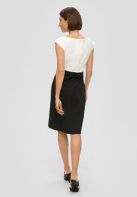 Robe noire et blanche avec une silhouette ajustée, des manches courtes, et un détail de fermeture éclair à l'arrière. Texture lisse, longueur au genou.