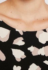 Svart topp med ett stort, abstrakt mönster i beige och kräm. Slät textur med vid halsringning och ingen synlig hårdvara.