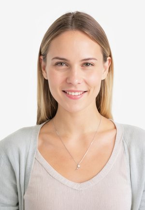 Silberne Halskette mit einem kleinen Anhänger, getragen über einem hellbeigen V-Ausschnitt-Oberteil und einer weichen grauen Strickjacke, die durch glatte Texturen und ein einfaches Design bestechen.