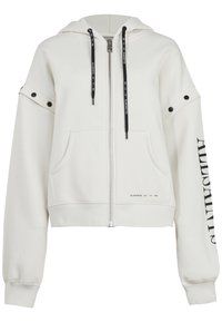 Vit kortärmad hoodie med dragkedja, två framfickor, svarta snoddar, tryckknappdetaljer på axlarna och en tryckt logotyp längs ärmen.