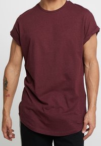 Camiseta de algodón color burdeos con mangas remangadas, escote redondo y ajuste relajado, con dobladillo curvo y textura suave.