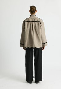 Gray, oversized jacket with black scalloped trim, featuring a high collar and drop shoulders. Paired with wide-leg black pants.
