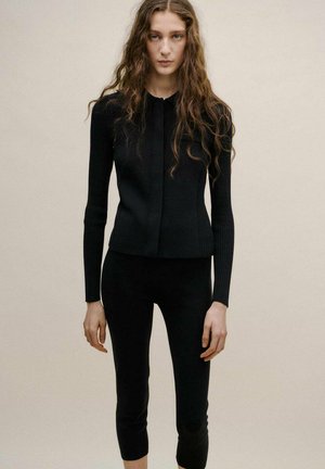 Top negro de punto con cuello alto, mangas largas acanaladas y silueta ajustada, combinado conleggings negros a juego que terminan en la pantorrilla.