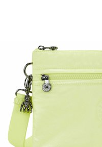 Borsa a tracolla in nylon verde lime con scomparto con zip, hardware in metallo e un piccolo charm a forma di scimmia attaccato al cursore della zip.