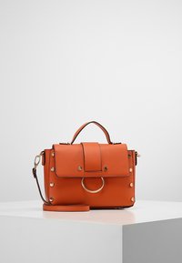 Sac à main en cuir orange avec une poignée supérieure, une bandoulière amovible, une fermeture à rabat, un accent en métal circulaire et des détails cloutés.