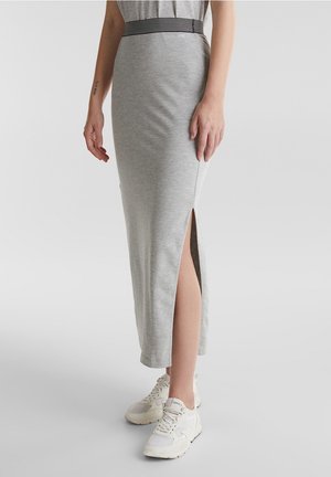 Mujer con falda midi ajustada gris claro con abertura lateral y zapatillas blancas sobre un fondo liso.