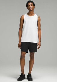 Vit ärmlös tanktop med en avslappnad passform, kombinerad med svarta shorts. Shortsen har en slät textur och en elastisk midja. Svarta sneakers.