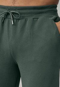 Dark green textured joggers with a ribbed waistband, adjustable drawstring, and side pockets, showcasing a solid color and subtle pattern.
