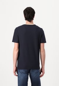 Tricou din bumbac de culoare albastru marin, cu un guler rotund clasic și mâneci scurte, prezentat din spate. Are o croială lejeră.