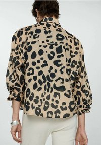 Chemise en tissu beige à imprimé léopard avec des taches noires, présentant une coupe ample, des manches longues et un col de chemise. Design léger et décontracté.