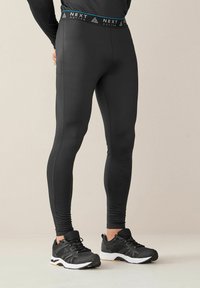 Sorte aktive tights med en tætsiddende design, der har en kontrasterende blå og sort talje mærket "NEXT ACTIVE." Glat tekstur, ingen mønstre.