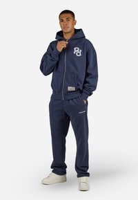 Navy hoodie with front zipper and logo on chest, paired with matching joggers. Features ribbed cuffs and a textured fabric.