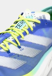 Baskets de sport bleues avec tige en mesh, rayures blanches et lacets jaunes vifs. Présentent une semelle épaisse et une languette perforée pour la respirabilité.