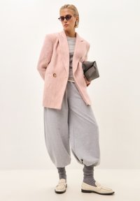 Rosa Wollmischungs-Blazer, grauer Sweatshirt, übergroße graue Sweatpants und cremefarbene Loafers. Zu den Accessoires gehören eine graue Clutch und lila Sonnenbrille.