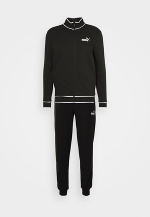 Tuta nera realizzata in tessuto morbido; presenta una giacca con zip e colletto rialzato e pantaloni coordinati, entrambi con dettagli e loghi bianchi.