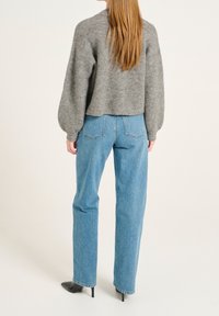 Grauer, gestrickter Pullover mit einem kurzen Design, kombiniert mit hochgeschnittenen, hellblauen Jeans. Schwarze, spitze Absätze runden das Outfit ab.