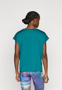 Τιρκουάζ μπλουζάκι με κοντά μανίκια, άνετη εφαρμογή, λεία υφή και στρογγυλή λαιμόκοψη, σε συνδυασμό με πολύχρωμο κολάν με λευκές ρίγες.