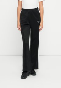 Μαύρο αθλητικό παντελόνι με άνετη εφαρμογή, διαθέτοντας μια λευκή λωρίδα κατά μήκος των πλευρών, ελαστική μέση και διακριτικό λογότυπο στην αριστερή πλευρά.