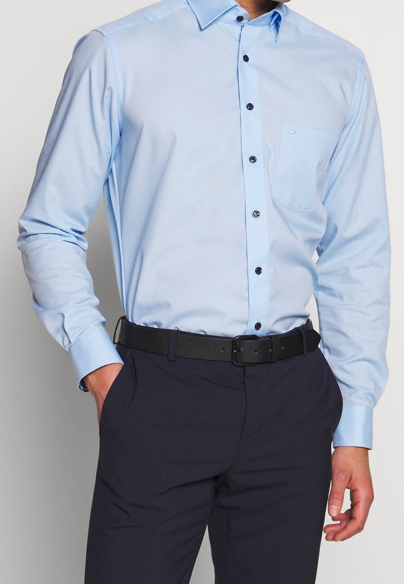 Lichtblauwe, langärmelige shirt met een button-down kraag, zwarte knopen en een borstzak. Draagt het met donkerblauwe broek en een zwarte riem.