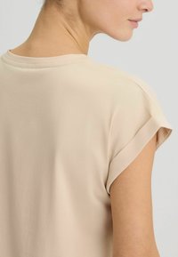 Top beige a maniche corte con risvolti, caratterizzato da una texture liscia e una vestibilità comoda, che presenta un design sottile e pulito.