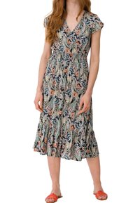 Kvinde iført en farverig paisley midi kjole med korte ærmer og en flæsekant, parret med lyst orange flade sandaler.
