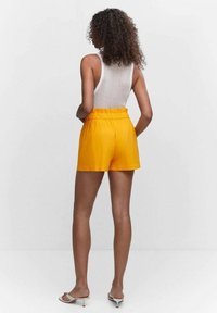 Pantaloni shorts gialli, leggeri, con una cintura elastica, progettati con una vestibilità rilassata. Il materiale sembra liscio, senza motivi visibili.