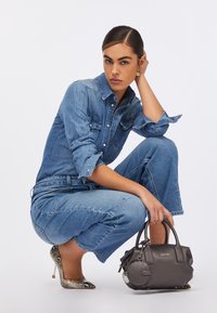 Geantă din piele gri, cu formă rotundă și două mânere, asortată cu o cămașă din denim și blugi evazați, purtând tocuri cu imprimeu de şarpe.