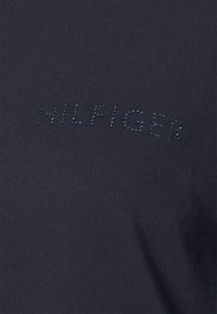 Tmavě modré tričko s hladkým, měkkým povrchem, které má na prsou slovo "HILFIGER" posázené třpytivými kamínky.