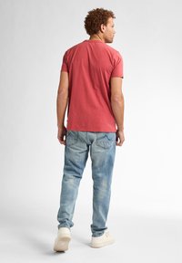 Camiseta de algodón roja de manga corta, combinada con unos vaqueros de mezclilla azul claro con un lavado desvaído y detalles en el bolsillo trasero.