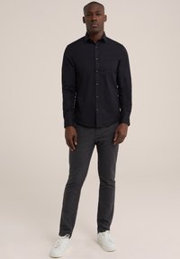 Chemise noire à manches longues, au design ajusté. Portée avec un pantalon gris à rayures et des baskets blanches. Texture du tissu lisse.