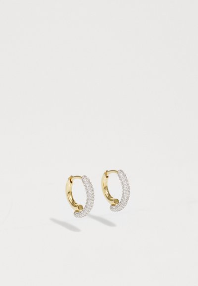 Guld hoops øreringe har et buet design prydet med små, klare sten langs den ydre kant, hvilket skaber en funklerende effekt.