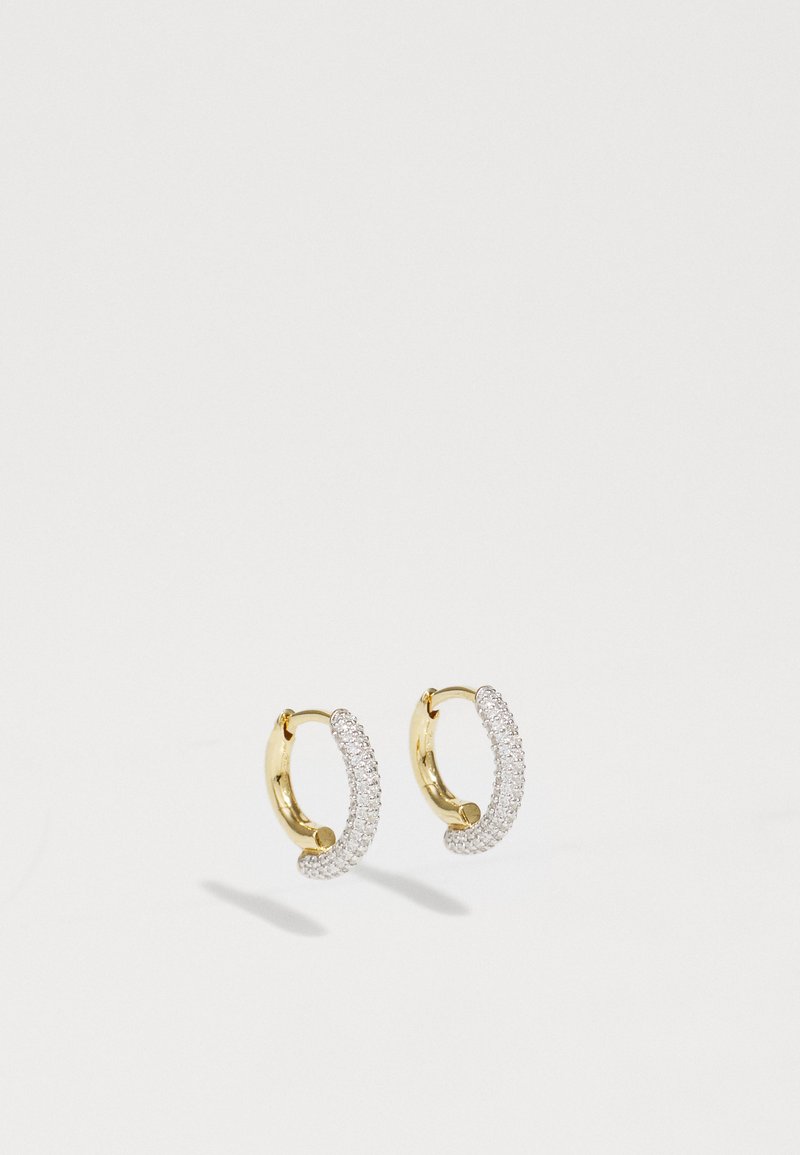 Zlatni kružni naušnice imaju zakrivljen dizajn ukrašen malim, prozirnim draguljima duž vanjskog ruba, stvarajući blistav učinak.