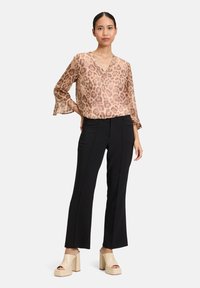Blusa a stampa leopardata color terra con maniche a campana abbinata a pantaloni neri su misura e tacchi a piattaforma beige. Tessuto morbido con una vestibilità comoda.
