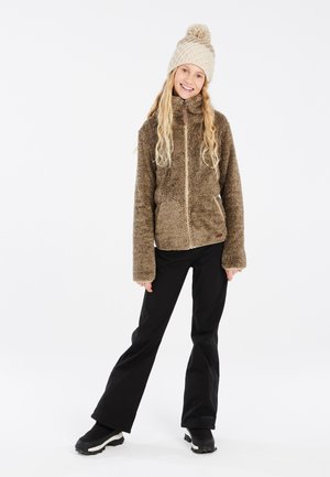 Braune Fleecejacke mit hohem Kragen, Reißverschluss und Seitentaschen, kombiniert mit schwarzen Schlaghosen und schwarzen Knöchelstiefeln.