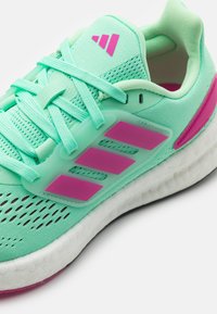 Světlé zelené sportovní boty s růžovými pruhy a logem, polstrovaný límec, pletený síťový svršek a bílá odpružená podrážka.