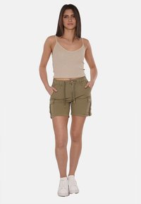 Pantaloni cargo verde oliva con molte tasche, vita con cordino e design aderente, abbinati a un top in cotone beige a coste e scarpe da ginnastica bianche.