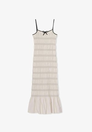 Ujjatlan, bézs ruha elasztikus redőzéssel, fekete díszítéssel és masni részlettel a dekoltázsnál; a ruha alján bővülő szegéllyel rendelkezik.