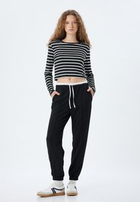 Zwart-wit gestreepte cropped top met lange mouwen, gecombineerd met losse zwarte joggers met een elastische tailleband en zijzakken. Witte sneakers.