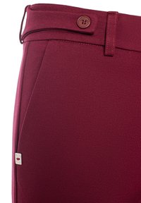 Pantalons ajustés bordeaux en tissu texturé avec une fermeture à bouton et des accents cousus. Présente une petite étiquette de marque sur le côté.