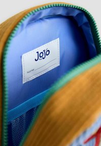 Orange tygutvändig med en blå nyloninredning, grön dragkedja och ett sydd namn etikett, utformad för organisatorisk förvaring.