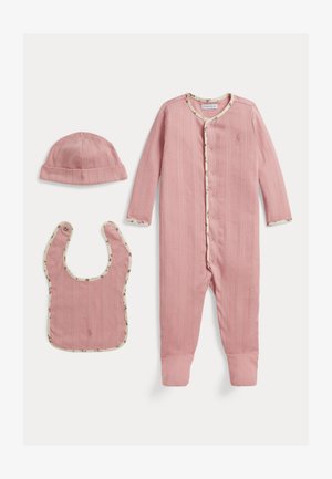 Bonnet bébé côtelé rose, bavoir et grenouillère à pieds avec bordure florale, disposés à plat sur fond blanc.