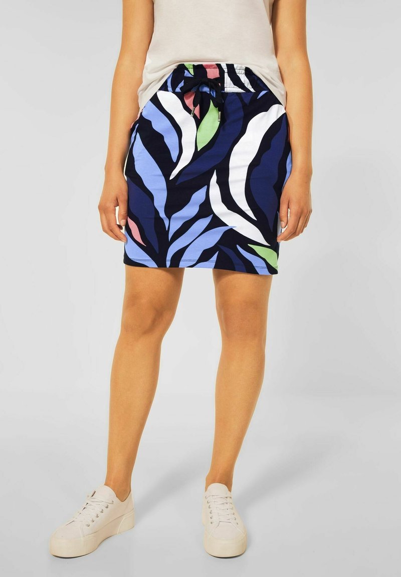 En marinblå kjol med ett lövmönster i grönt, vitt och ljusblått, med elastisk midja och dragsko. Bärs med vita sneakers.