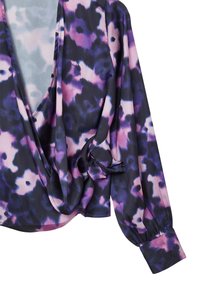 Blouse à motif floral violet et rose, avec un décolleté en V profond, un devant drapé et des manches longues à poignets froncés. Tissu lisse et léger.