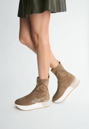 Stivaletti alla caviglia in suede color sabbia con dettaglio a stella, suola bianca e accento dorato sul tallone; design snello e aderente.