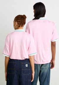 Camisa polo de manga curta rosa com um padrão geométrico subtil, com contraste em verde e branco nos colarinhos e punhos.