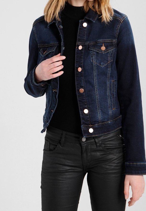 Mörk denimjacka med en figurnära passform, bronsdetaljer, bröstfickor och knappstängningar. Bärs över en svart stickad topp och svarta byxor.