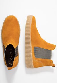 Des chaussures slip-on en daim jaune avec des panneaux élastiques sur les côtés et une semelle en caoutchouc beige texturée. Elles présentent un doublure à motifs noir et blanc.
