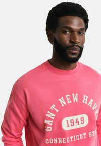 Felpa rosa in cotone con scollatura rotonda, caratterizzata da testo stampato bianco: "GANT NEW HAVEN 1949 CONNECTICUT STATE" in carattere in grassetto.