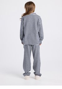 Ensemble de pyjama à carreaux bleu marine et blanc ; chemise ample avec col à boutons et manches longues, pantalon assorti avec poignets élastiques et texture douce.